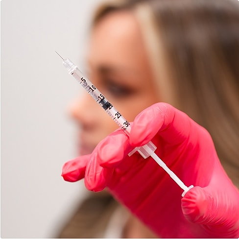 Medical professional holding a syringe with pink gloves.