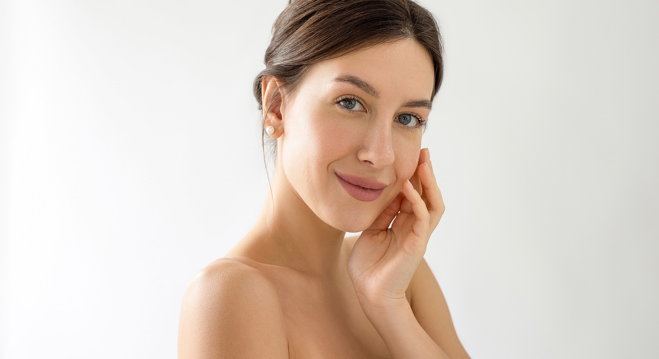 Woman touching her face, smiling against white background.