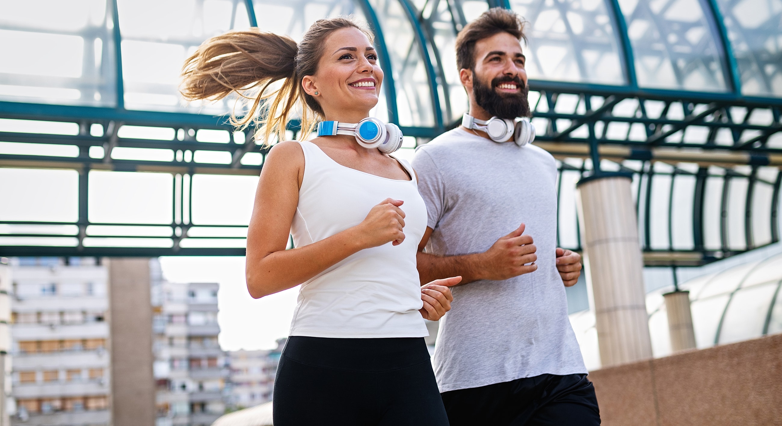 Couple jogging with headphones outdoors, smiling.